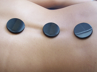 close up photo of person's back with three round massage stones thumbnail
