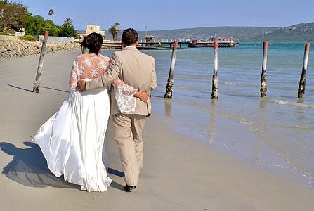 newlywed couple walking on seashore under blue sky at daytime thumbnail
