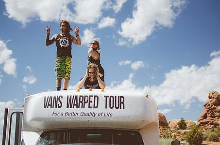 three people standing on Vans Warped Tour RV in distant of rock mountains thumbnail