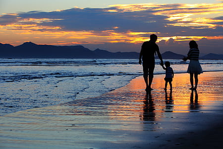 man, woman, and toddler walking on the seashore during golden hour thumbnail