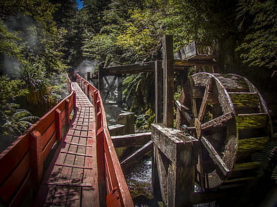 red steel suspension bridge besides brown water mill thumbnail