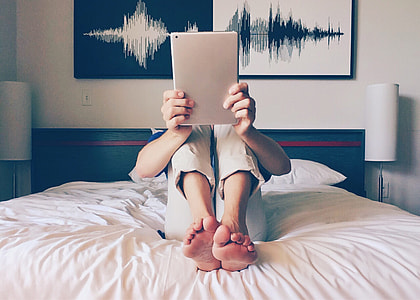 person in beige jeans using iPad while sitting on white bed thumbnail