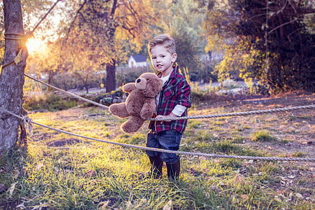boy carrying bear plush toy holding onto a rope attached to trees thumbnail