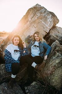 two women in blue jackets sitting on brown rock formation thumbnail
