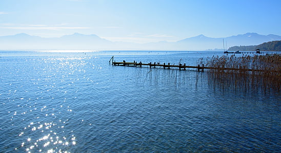 brown and black dock between body of water near mountains under white and blue sky at daytime thumbnail