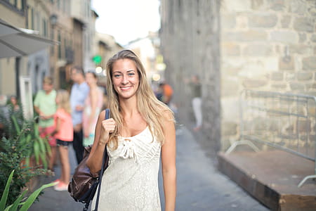 A young blonde woman in white dress carrying a leather bag posing in the street thumbnail