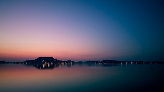 silhouette of mountain near calm sea during dawn thumbnail