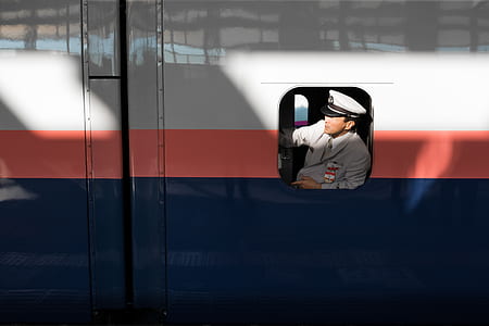man wearing grey jacket inside white, red, and blue train thumbnail