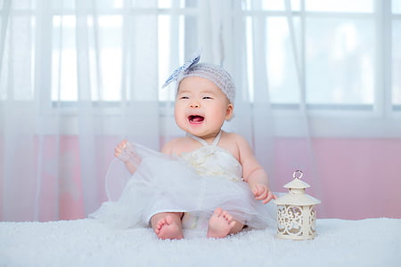 baby smiling while sitting on white textile thumbnail