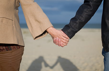 man and woman holding hands on seashore near beach thumbnail