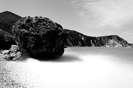 grayscale photo of body of water beside mountain thumbnail