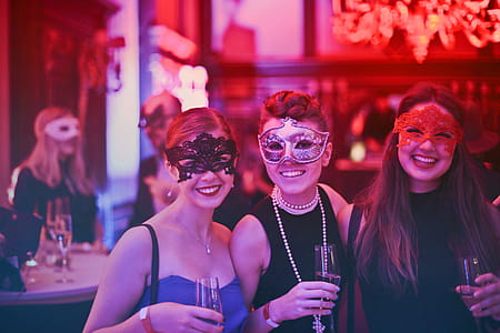 Three Women In Masks Posing While Holding Wine Glasses In Nightclub thumbnail