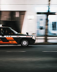 man drives black, white, and orange car passing by on black asphalt road thumbnail