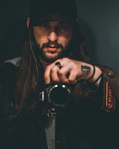 shallow focus photography of man holding his camera while taking a picture thumbnail