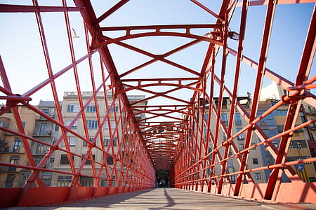 A red caged-design walking bridge with building apartments in the background thumbnail