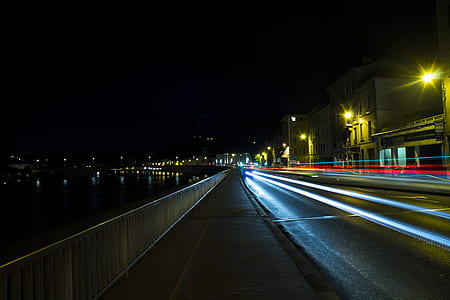 time-lapse photography of vehicle lights on road beside buildings and body of water during nighttime thumbnail