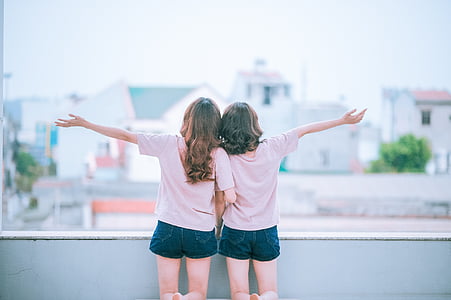 girl wearing white crew-neck shirt beside girl raising right arm thumbnail