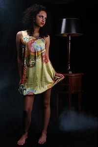 woman wearing green, red, and blue mini dress beside table with lamp thumbnail