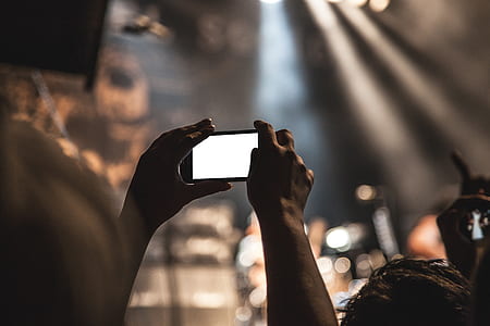 selective focus photography of person holds smartphone in portrait mode during concert thumbnail