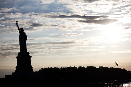 silhouette of Statue of Liberty under white clouds at golden hour thumbnail