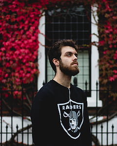 man wearing Oakland Raiders top in front of red petaled trees thumbnail