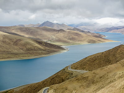 mountains covered with trees near body of water under gray clouds during daytime thumbnail