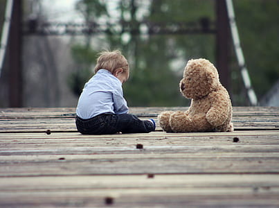 boy sitting next to brown bear plush toy during daytime thumbnail