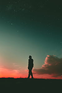 silhouette photo of a man standing on grass under cloudy sky during golden hour thumbnail