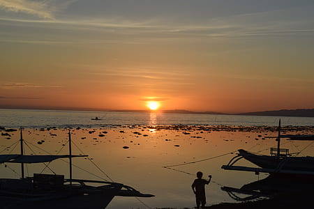 silhouette photo of person near fishing boats on a shore during golden hour thumbnail