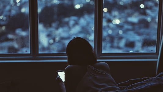 woman holding smartphone while lying on bed with boke lights background thumbnail