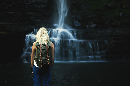 shallow focus photography of woman wearing gray backpack in front waterfalls thumbnail
