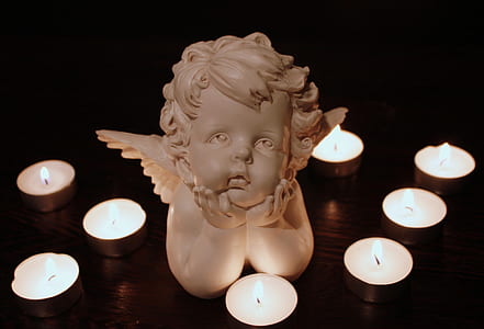 white cherub figurine besides candles inside dark room thumbnail