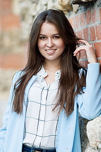 smiling woman standing beside brown bricked wall during daytime thumbnail
