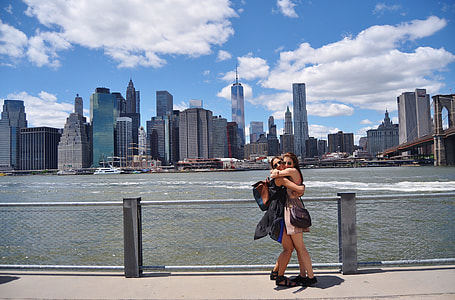 photo of two women hugging near wire fence under gray clouds during building faraway from Empire State building New York thumbnail