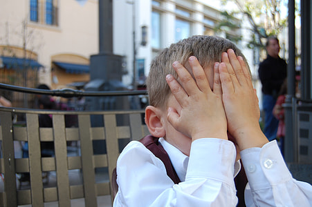 boy wearing white dress shirt while sitting on chair and close his eyes using his hands during day time thumbnail