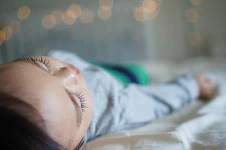 bokeh photography of baby sleeping wearing gray sweater lying down on top of white textile thumbnail