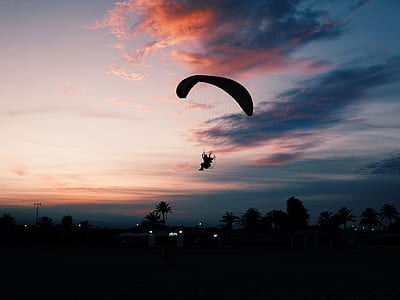 silhouette photo of man skydiving landing on land at noontime thumbnail