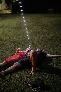 Man and Woman Lying on Green Grass Holding String Lights thumbnail