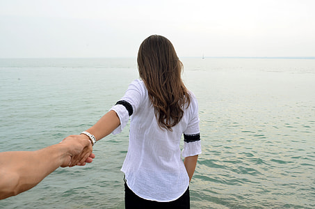 woman and person holding hands near body of water during daytime thumbnail