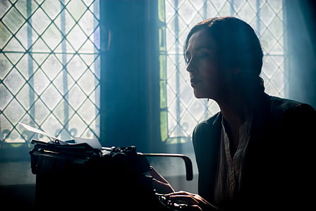 woman in black top looking into black typewriter thumbnail