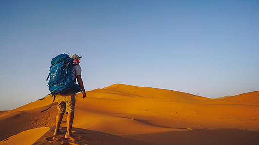 man with blue backpack standing on dessert at daytime thumbnail