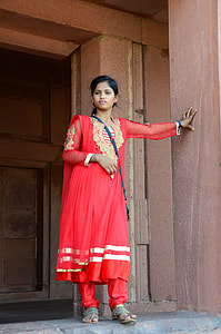 woman in red abaya standing next to brown concrete wall thumbnail