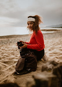 woman holding phone while kneeling on beach sand beside her bag thumbnail