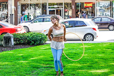 Woman in White Sleeveless Shirt and Blue Pants Holds Yellow Hula Hoop Stands on Green Grass thumbnail