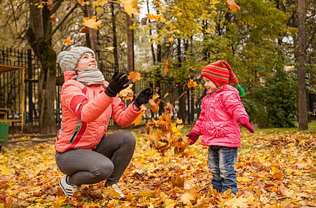 woman in red sweater tossing upward some brown leaves while a girl playing with it thumbnail