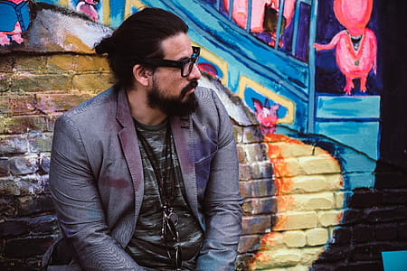 Man Wearing Black Eyeglasses Sitting Near Wall With Murals thumbnail