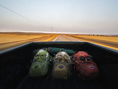 three orange, brown, and green hiking backpack on pickup truck thumbnail