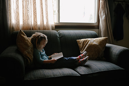 girl sitting on sofa reading book beside closed window thumbnail