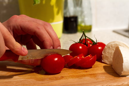 person slices red tomato on wooden chopping board thumbnail