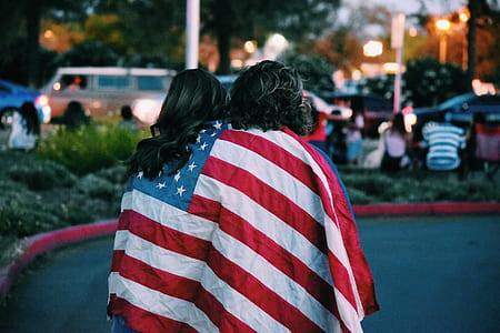 selective focus photography of couple walking on road with American flag on their back thumbnail